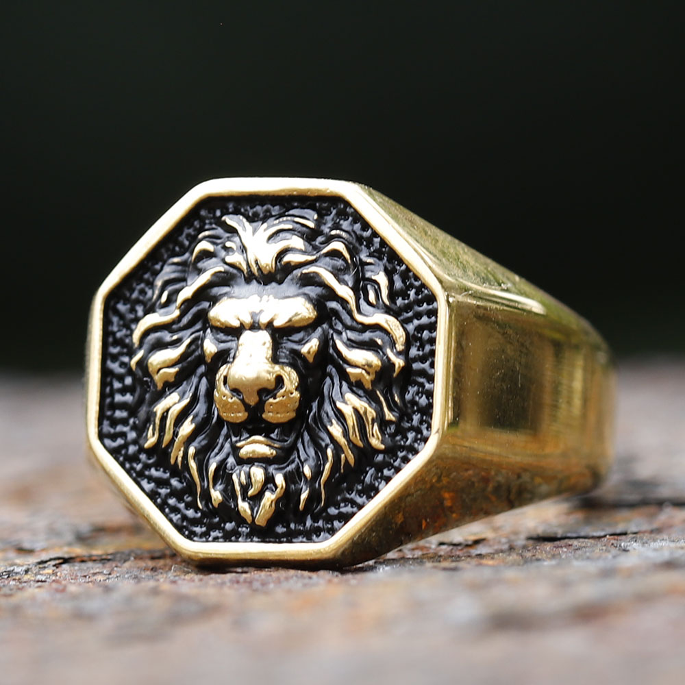 Detailed 3D lion head stainless steel ring, gold tone with black accents, on a rustic dark surface.