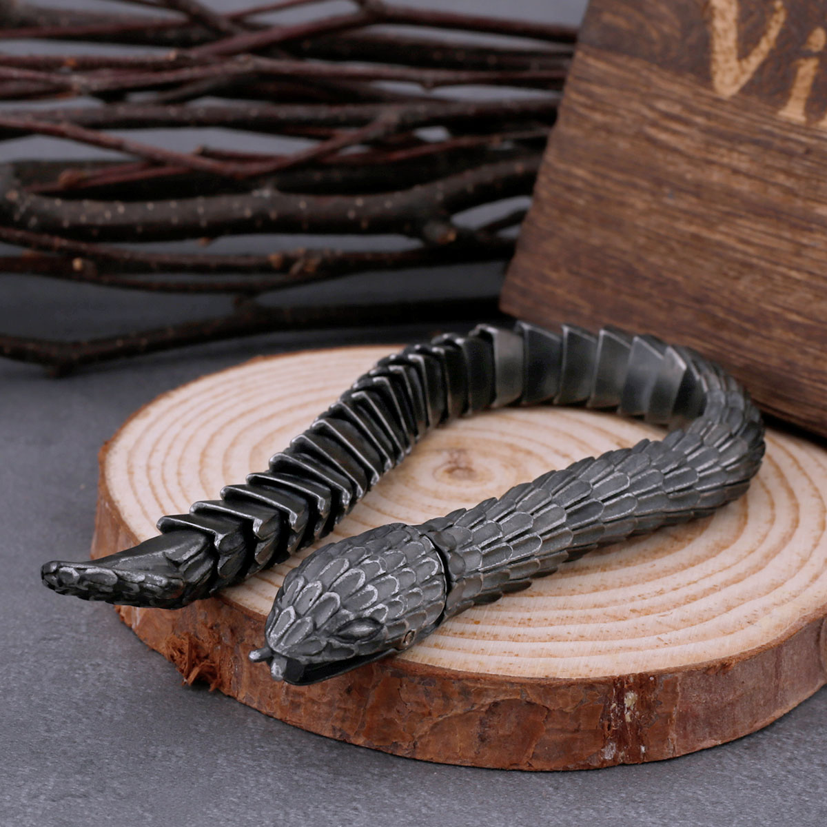 Detail of the bracelet's textured snake scale links, with blurred natural branches in the background, highlighting craftsmanship.