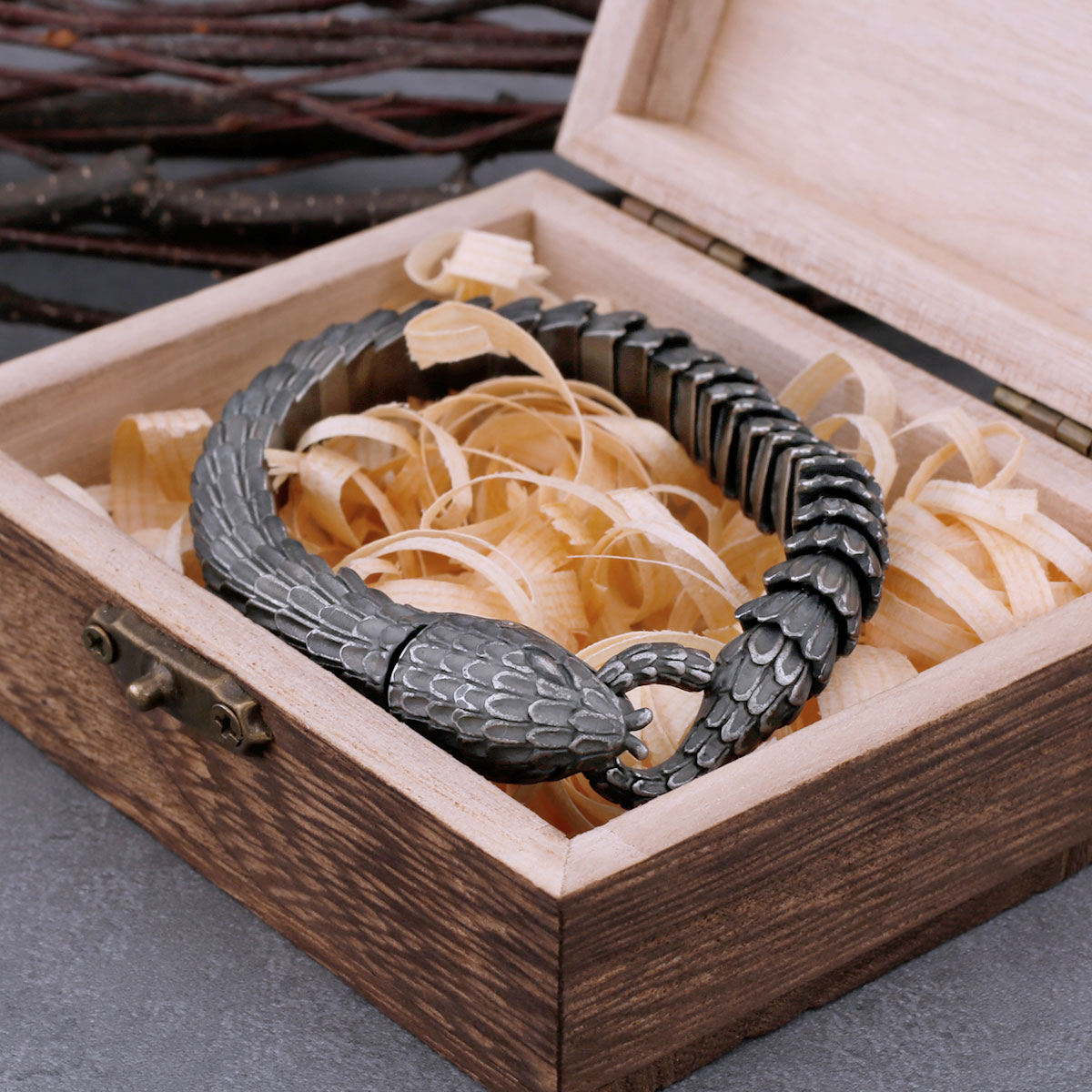 View of the coiled snake bracelet, emphasizing the connection of the serpent's head and tail clasp on a light wooden base.