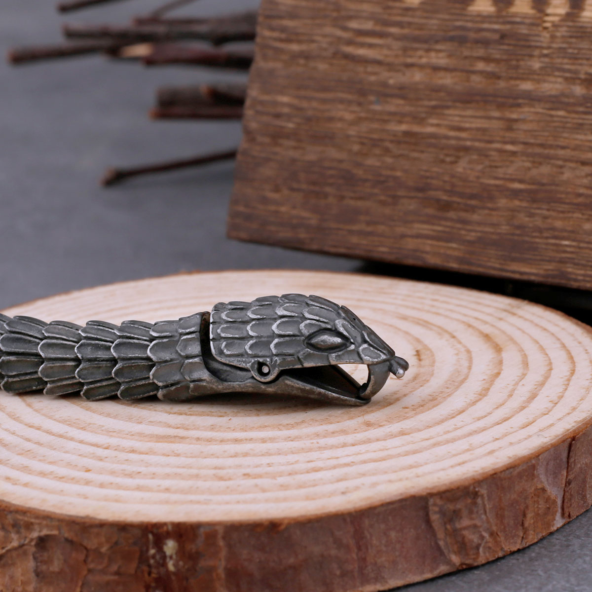 Angled view of the antique-finished Ouroboros snake bracelet, showing its full length and a blurred wooden box in the background.