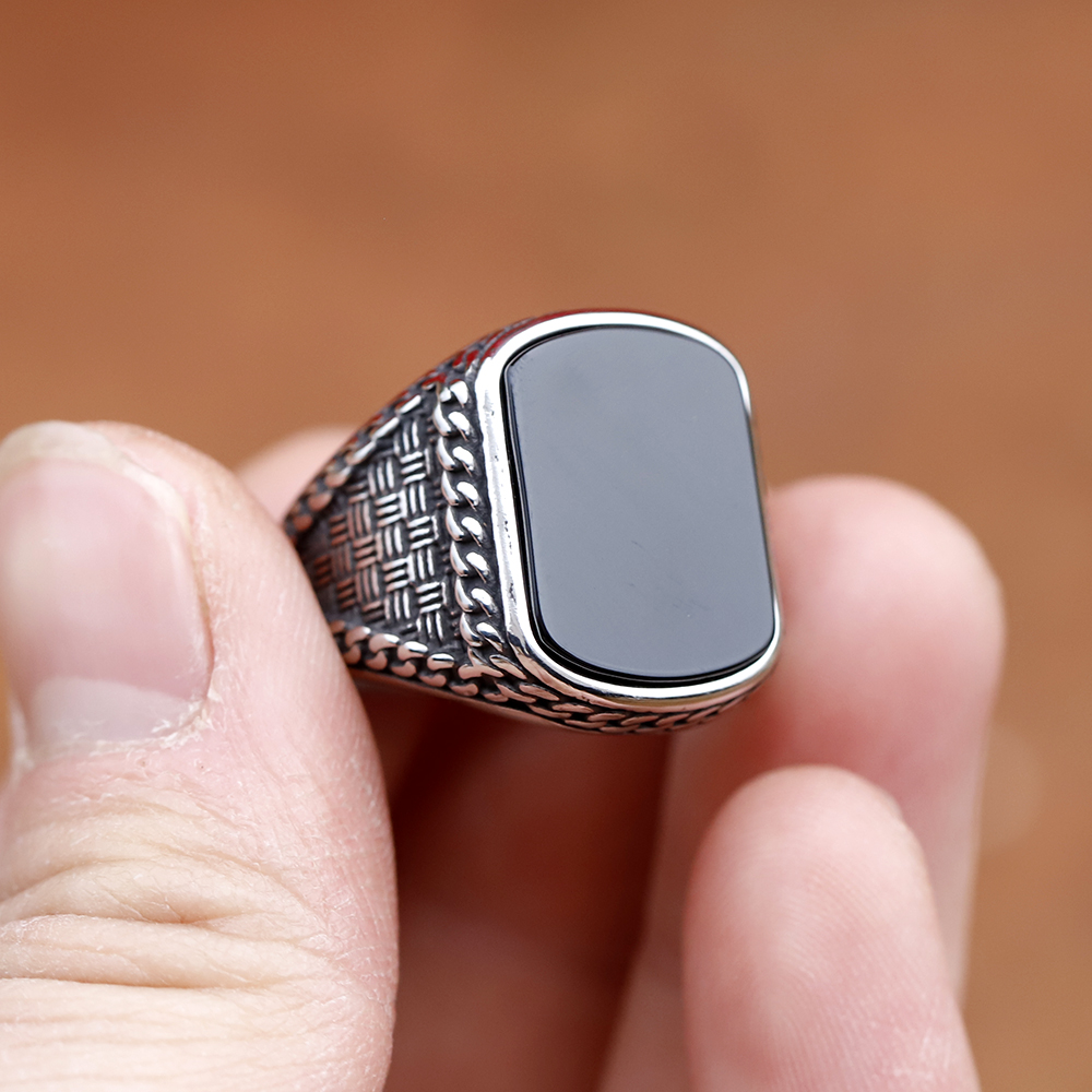 Full view of the robust stainless steel rectangle black stone ring against a rustic background.