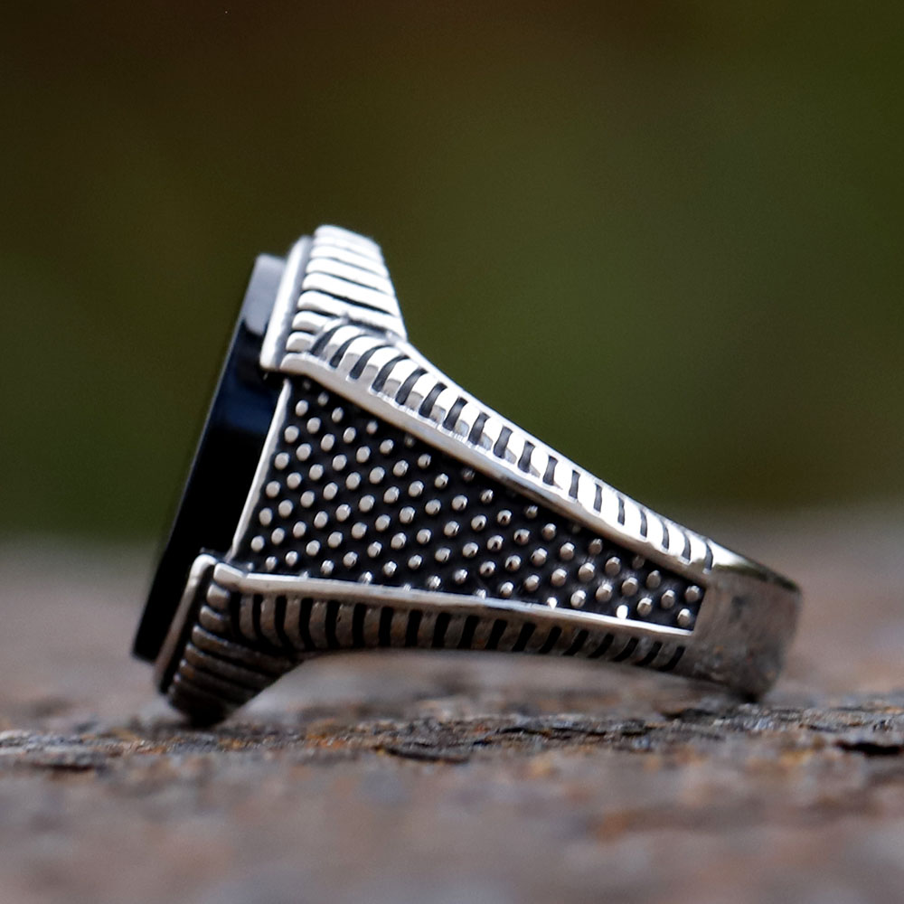 Side profile of the men's geometric black stone ring on a rustic surface