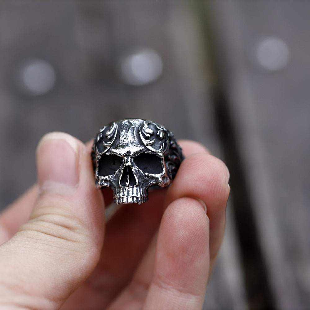 Angled close-up showcasing the side profile and elaborate scroll designs of the men's skull ring.
