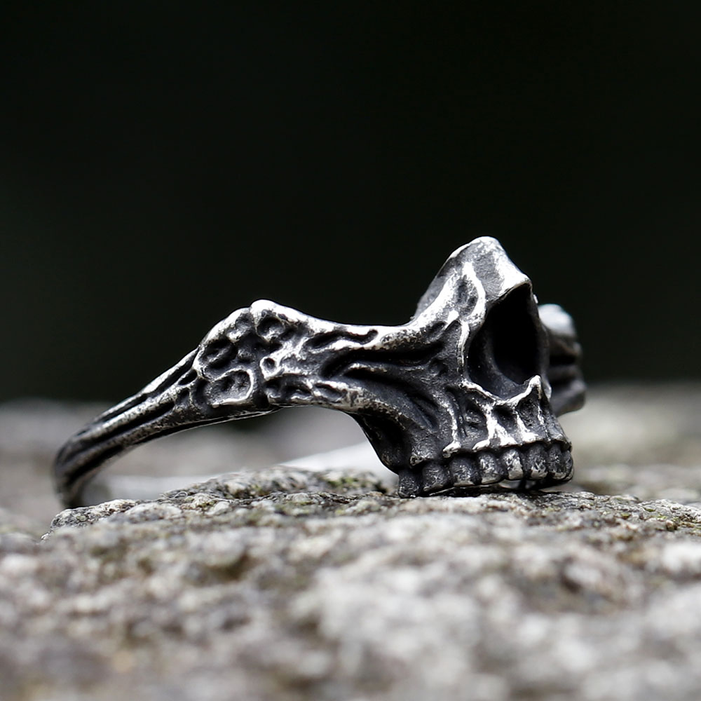 Oblique view of the durable steel skull ring, with a blurred dark background.