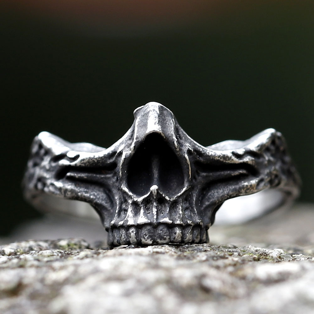 Close-up of a vintage gothic steel skull ring on a textured rock surface.