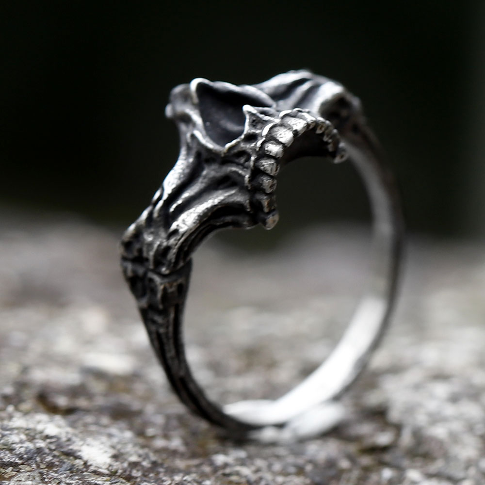Vintage style skull ring made of steel, resting on a rustic outdoor surface.
