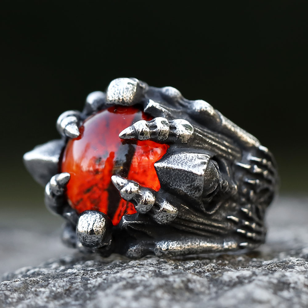 Close-up of a men's 316L stainless steel punk skull ring with a large central red stone on a dark gray rock.