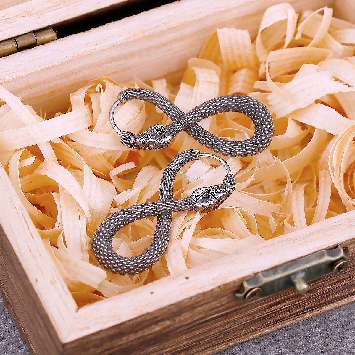 Close-up of the left snake earring's head and hoop closure against a light wood background.